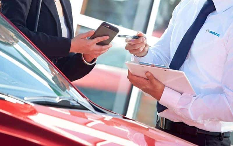 Couple is talking to Mazda Dealership Employee inside of showroom. 