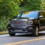 A black 2016 GMC Sierra 1500 Denali is shown driving down a road after leaving a used GM dealership.