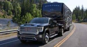 A black 2023 GMC Sierra 3500HD Denali is shown towing a large camper trailer on an open road.