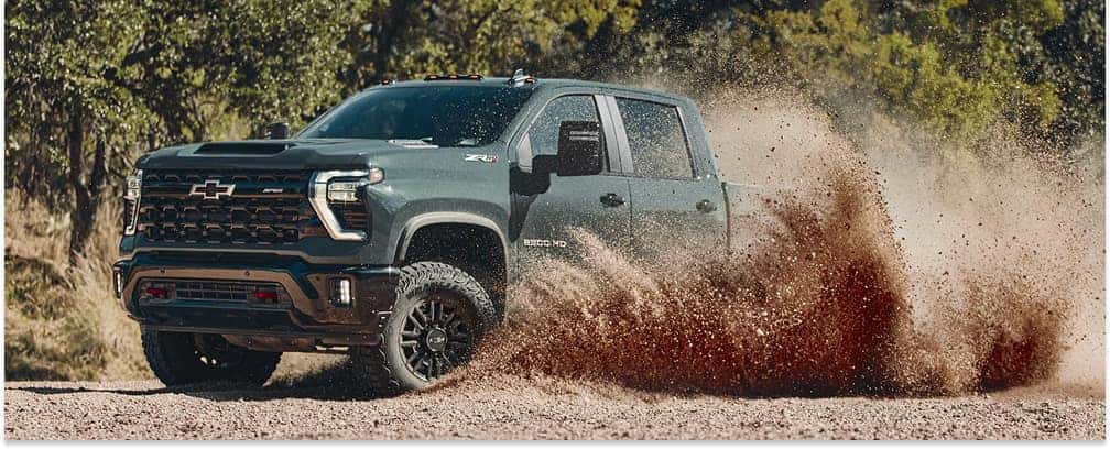 Gray 2026 Chevrolet Silverado HD ZR2 driving off-road and splashing dirt on a trail.