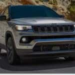 Front three-quarter view of a silver 2026 Jeep Compass driving on a mountain road.