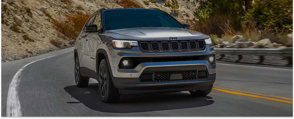 Front three-quarter view of a silver 2026 Jeep Compass driving on a mountain road.