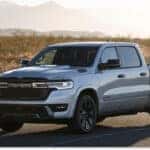Front three-quarter view of a silver 2026 RAM 1500 pickup truck parked on a desert road.
