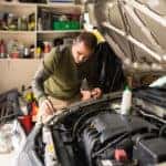A man working on his used car in the garage changing motor oil