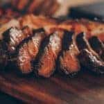 A row of BBQ brisket cooked to a perfect medium rare sitting on a wooden cutting board.