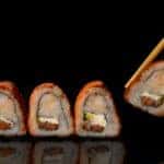 Sushi rolls lined up on a plate and being taken away with chopsticks