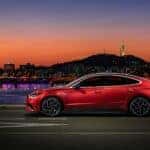 A red Hyundai Sonata at night in front of a lit skyline and the river.