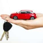 A hand holding a small red toy car and a ring of car keys.