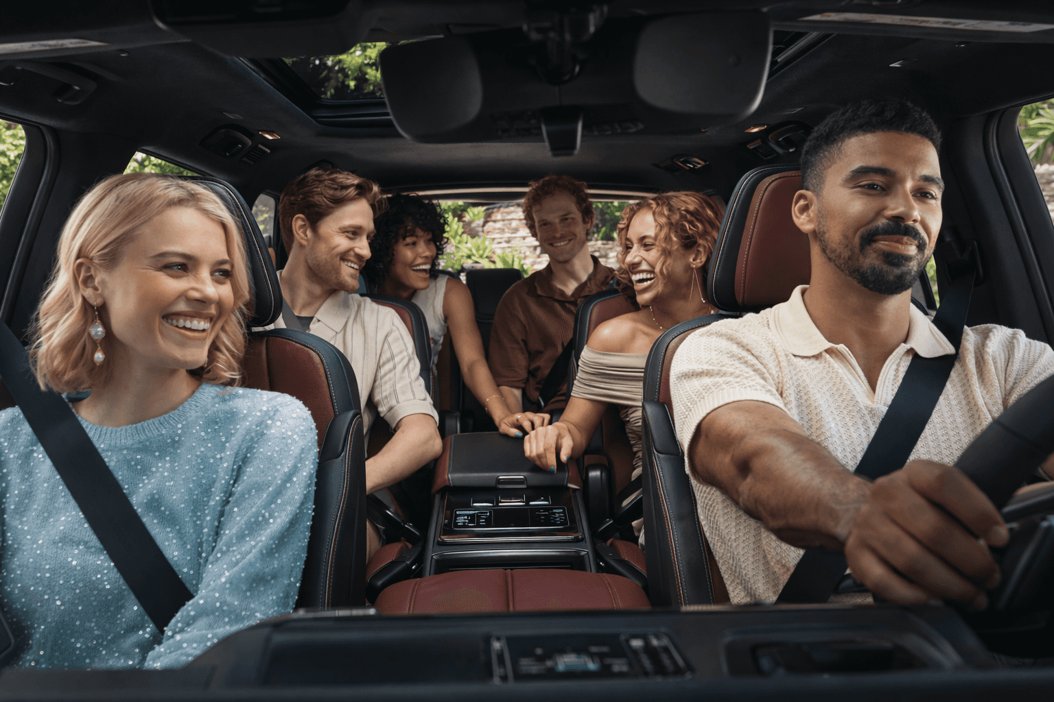 Interior of the 2026 INFINITI QX80 featuring red and black leather seats, panoramic sunroof, and a group of passengers enjoying spacious first-, second-, and third-row seating.