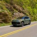 Avocado green 2026 Volkswagen Tiguan SEL R Line driving on the road next to a mountain