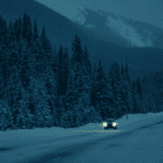 Car driving down a winter road in the mountains with snow covering the road and trees