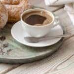 Brewed coffee in a white cup with delicious donuts on a wooden table close-up