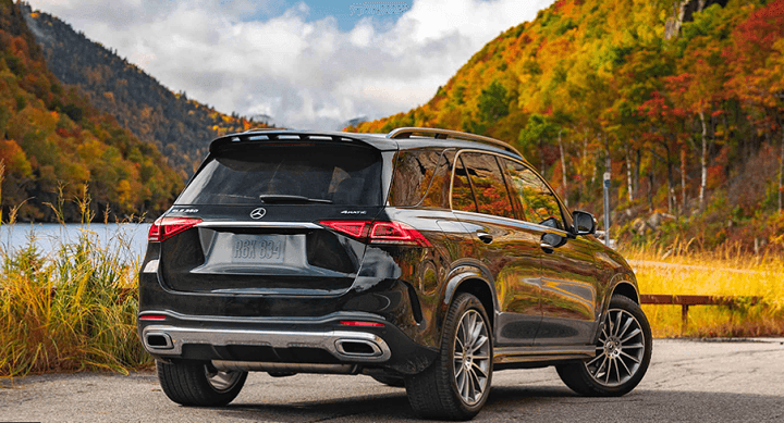 Black Mercedes-Benz GLE parked on the side of the road with a lake and mountains in the background with trees that have fall leaves