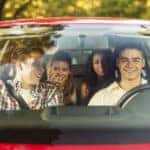 Four young people sitting in a car, going on vacation. Two males and two females, all Caucasian in their 20s.