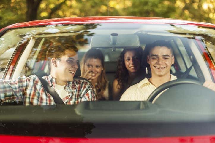 Four young people sitting in a car, going on vacation. Two males and two females, all Caucasian in their 20s.
