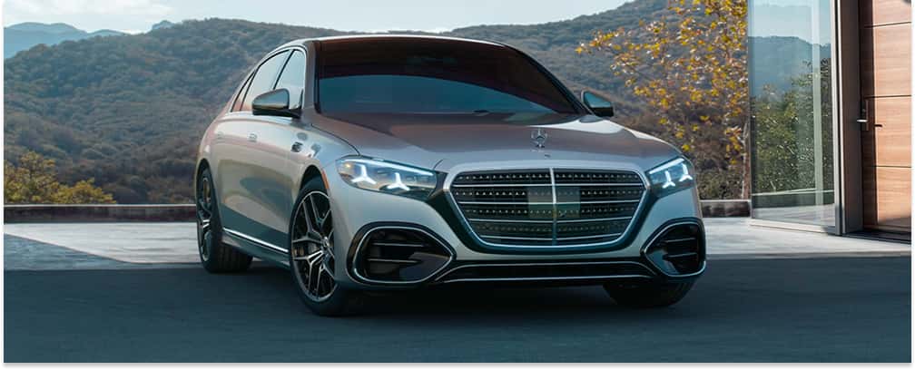 Front three-quarter view of a silver 2026 Mercedes-Benz S-Class sedan parked outside a modern home.