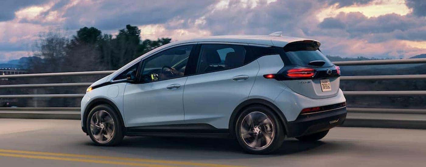 A light blue 2022 Chevy Bolt EV driving on a highway bridge at sunset.