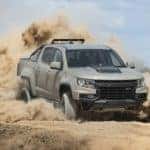 A tan 2022 Chevy Colorado ZR2 kicks up clouds of sand while off-roading in a desert.