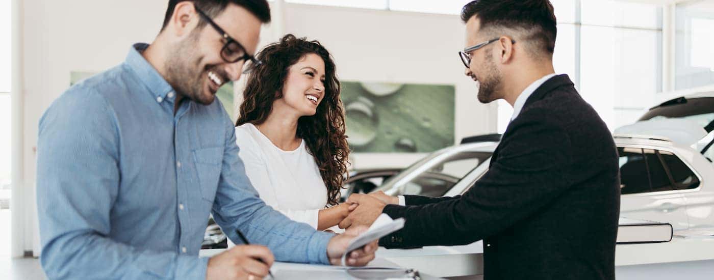 A salesman shaking hands with a couple after they traded in their car at the dealership