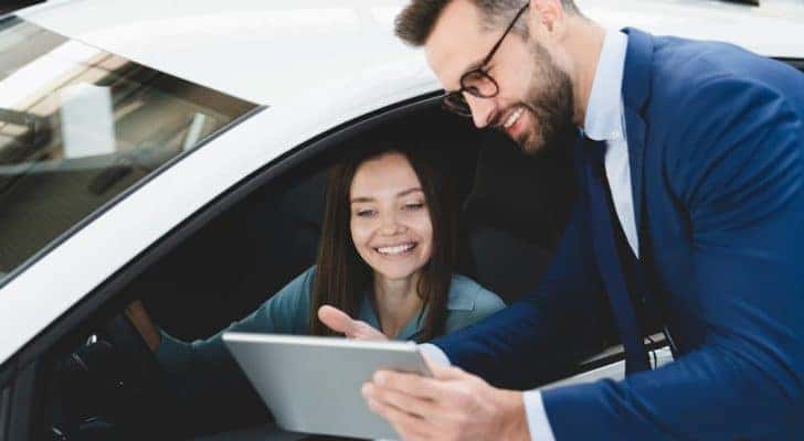A salesman leaning down to talk to a woman in her car.