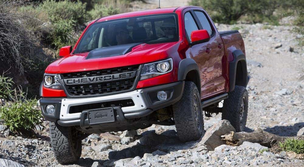 A red 2019 Chevy Colorado ZR2 Bison off-roading over uneven rocks in the desert