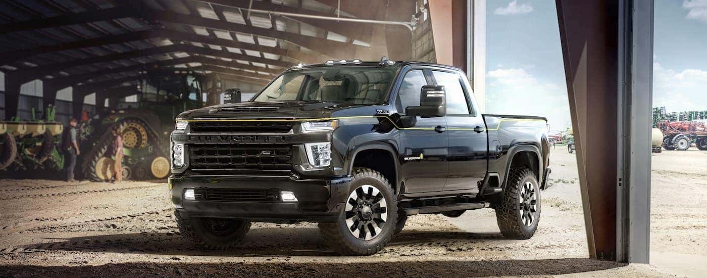A black 2021 Chevy Silverado 2500 HD Carhartt Edition parked in a hanger with large farm equipment.