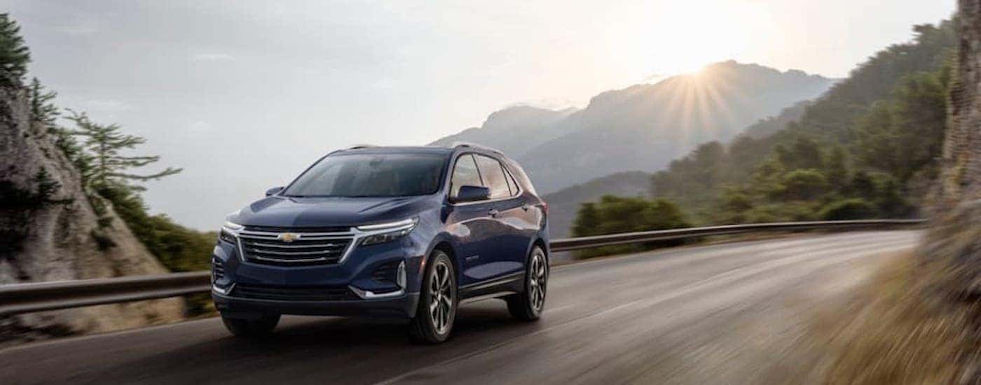 A certified chevy for sale, a blue 2020 Equinox Premier, driving on a mountain highway.