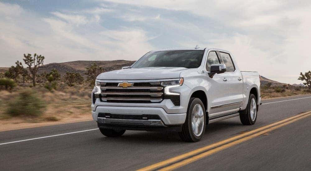 A white 2023 Chevy Silverado 1500 High Country driving down an open desert highway