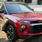 A red 2023 Chevy Trailblazer RS parked on the side of a city street near flowering trees