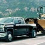 A black 2021 Chevy Silverado 3500 HD towing heavy machinery on a mountain highway.
