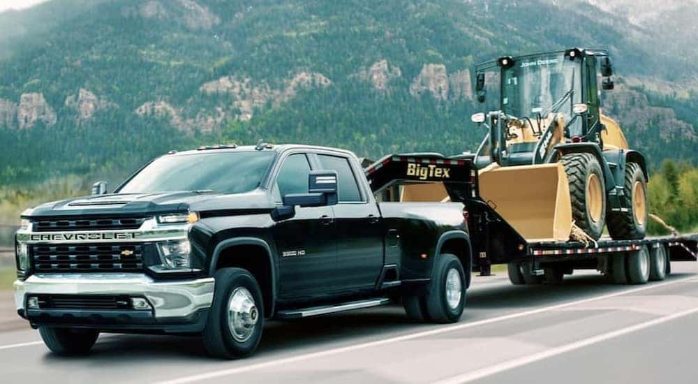 A black 2021 Chevy Silverado 3500 HD towing heavy machinery on a mountain highway.