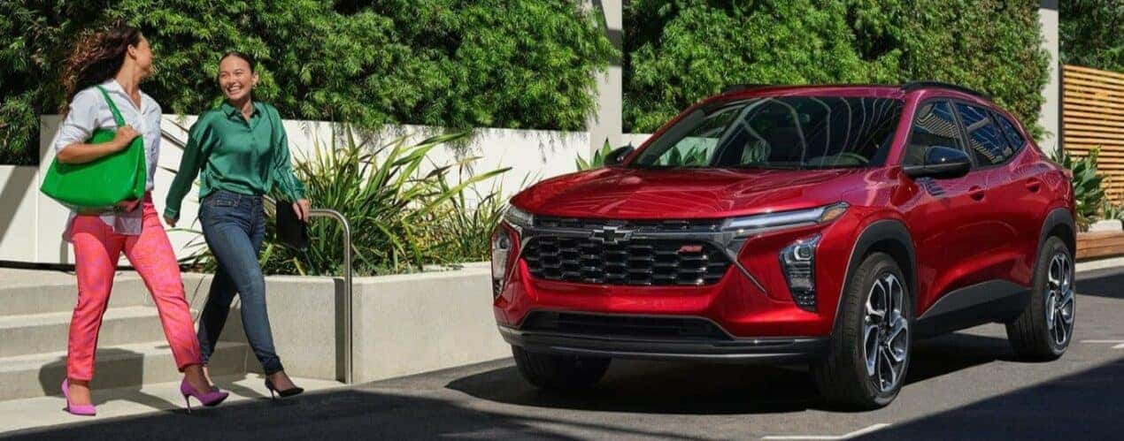 People are shown walking past a red 2024 Chevy Trax RS.