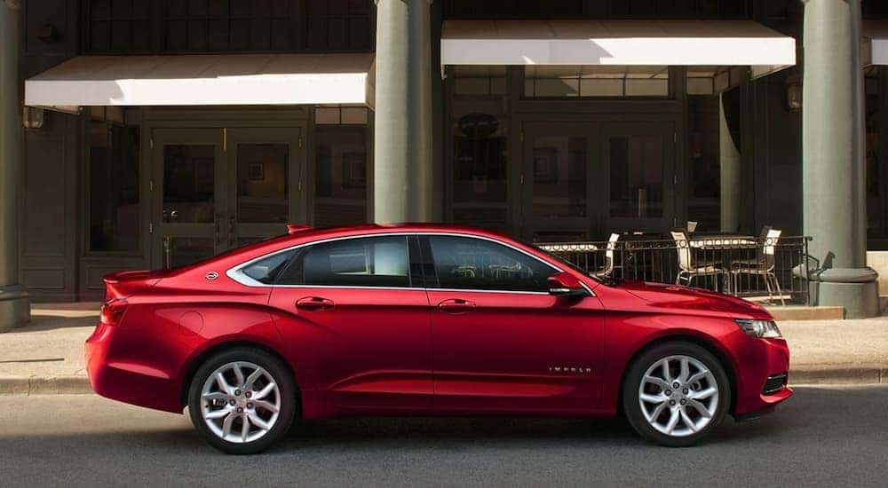 A red 2019 Chevy Impala is shown parked on a city street in front of outdoor cafe tables.
