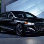 A black 2020 Chevy Malibu Midnight Edition is shown parked in front of a modern building at night.