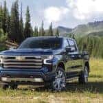 A blue 2022 Chevy Silverado 1500 High Country parked in a grassy meadow with mountains in the distance