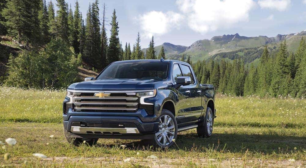 A blue 2022 Chevy Silverado 1500 High Country parked in a grassy meadow with mountains in the distance