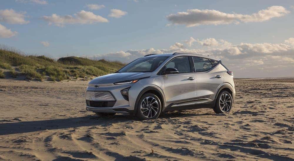 A silver 2022 Chevy Bolt EUV parked on a sandy beach with dunes in the background