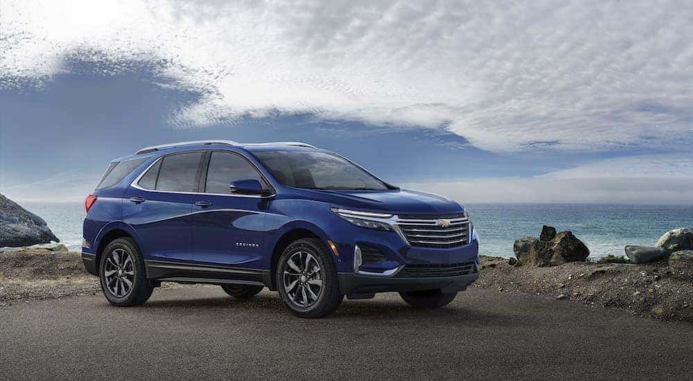 A blue 2023 Chevy Equinox Premier parked at a rocky ocean shoreline