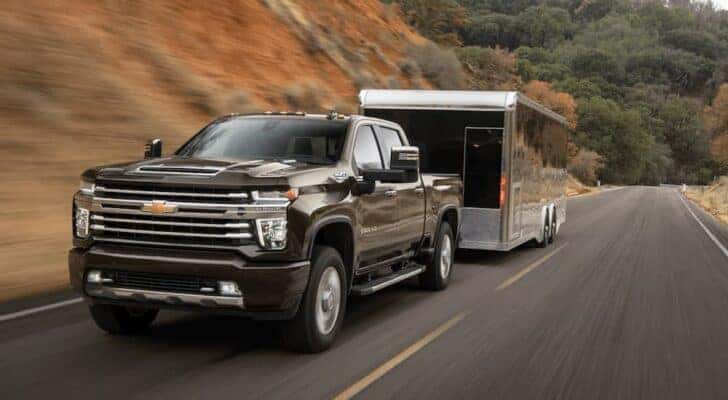 A brown 2023 Chevy Silverado 2500 HD is shown towing a black trailer on an open road.