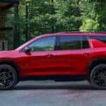 A red 2024 Chevy Traverse parked in front of a rustic garage in the woods