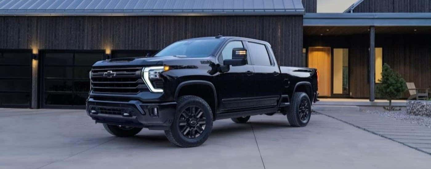 A black 2024 Chevy Silverado 2500 HD High Country is shown parked near a house.