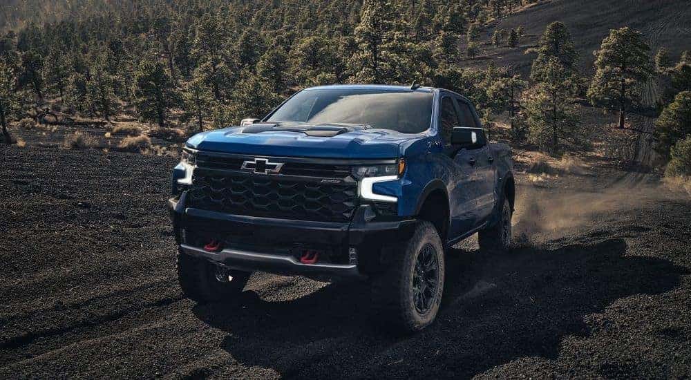 A blue 2024 Chevy Silverado 1500 ZR2 is shown driving off-road during a 2024 Chevy Silverado 1500 vs 2024 Ford F-150 competition.