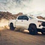 A white 2024 Chevy Silverado 1500 Trail Boss is shown from the front at an angle while off-road after leaving a dealer that has a Chevy Silverado for sale.