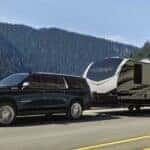 A dark blue 2024 Chevy Suburban High Country towing a camper through the mountains.