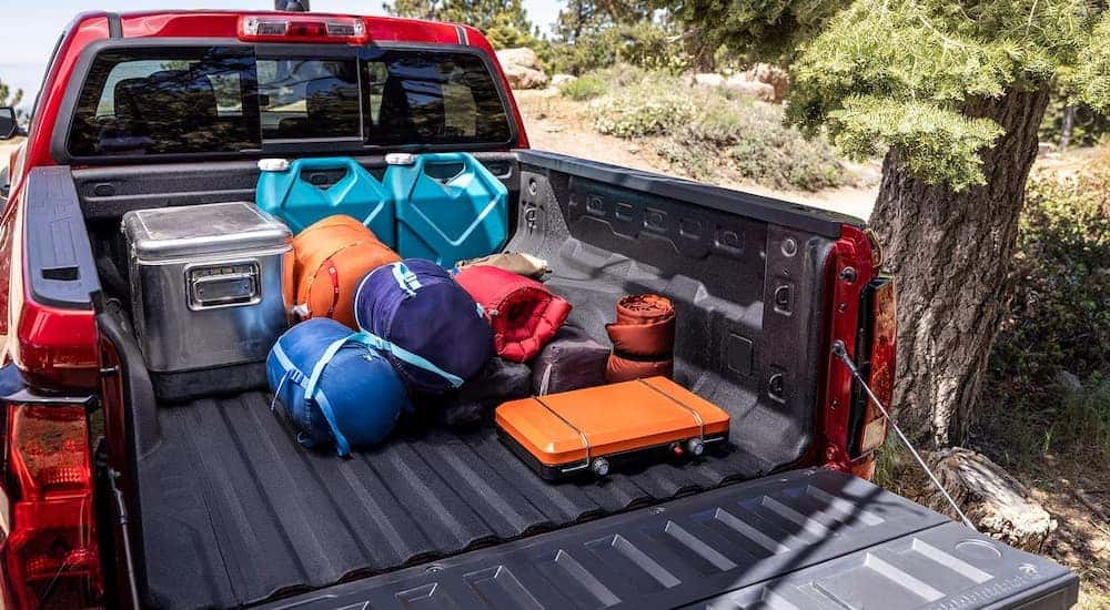 A red 2024 Chevy Colorado Trail Boss parked in the woods with camping gear in the bed.