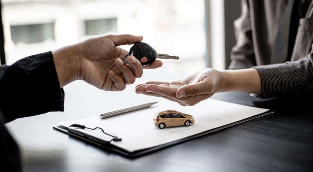 A customer is shown handing their car key to a salesman after selling their car.