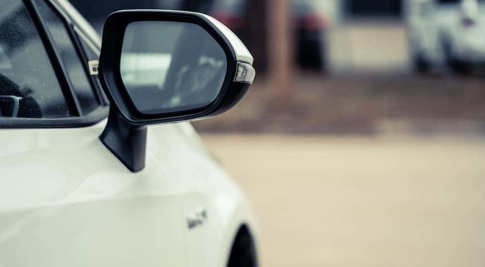 A close up of the side mirror on a white sedan is shown.