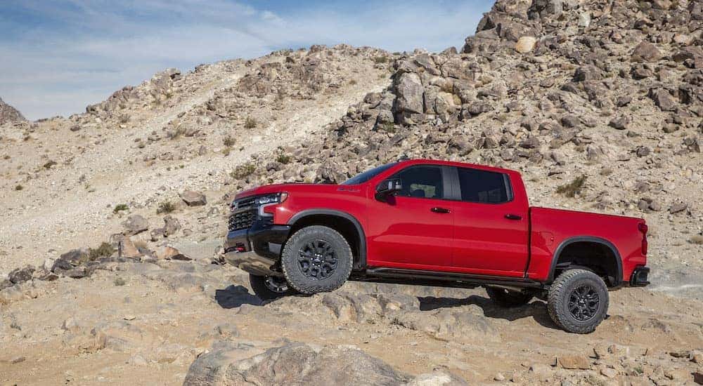 A red 2023 Chevy Silverado 1500 ZR2 is shown from the side while driving over a rock after leaving a Chevy Silverado 1500 dealer.