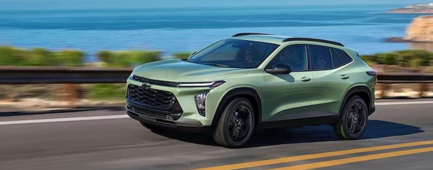 A green 2024 Chevy Trax is shown driving near the ocean.