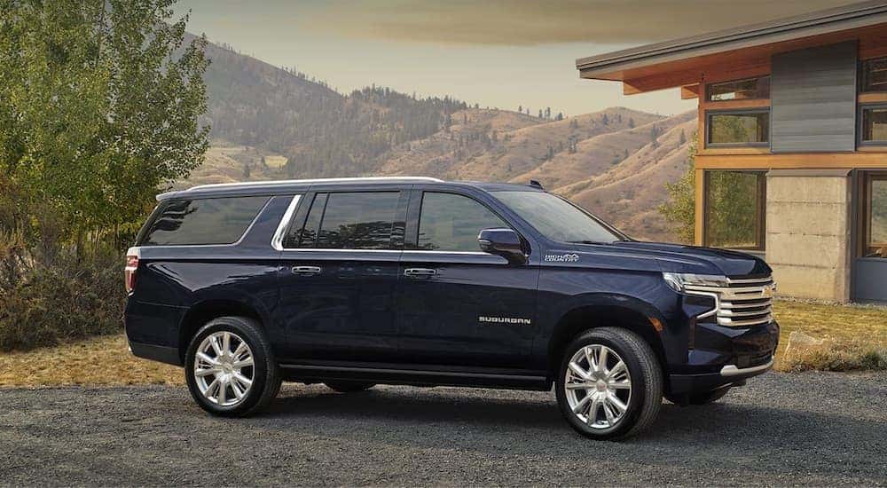A blue 2024 Chevy Suburban High Country is shown parked near a building.